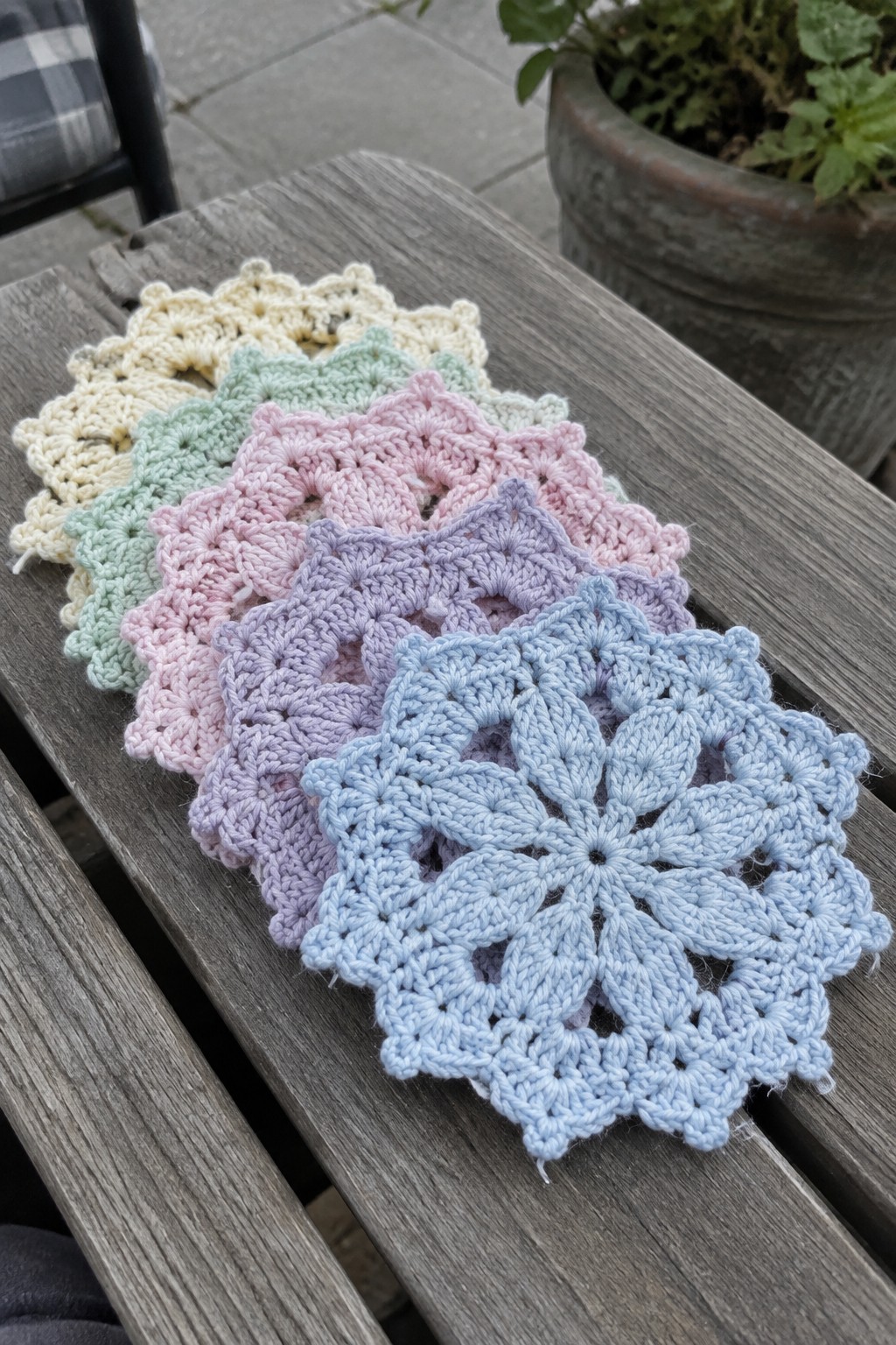 Pastel crocheted doilies fanned across a weathered wooden outdoor table