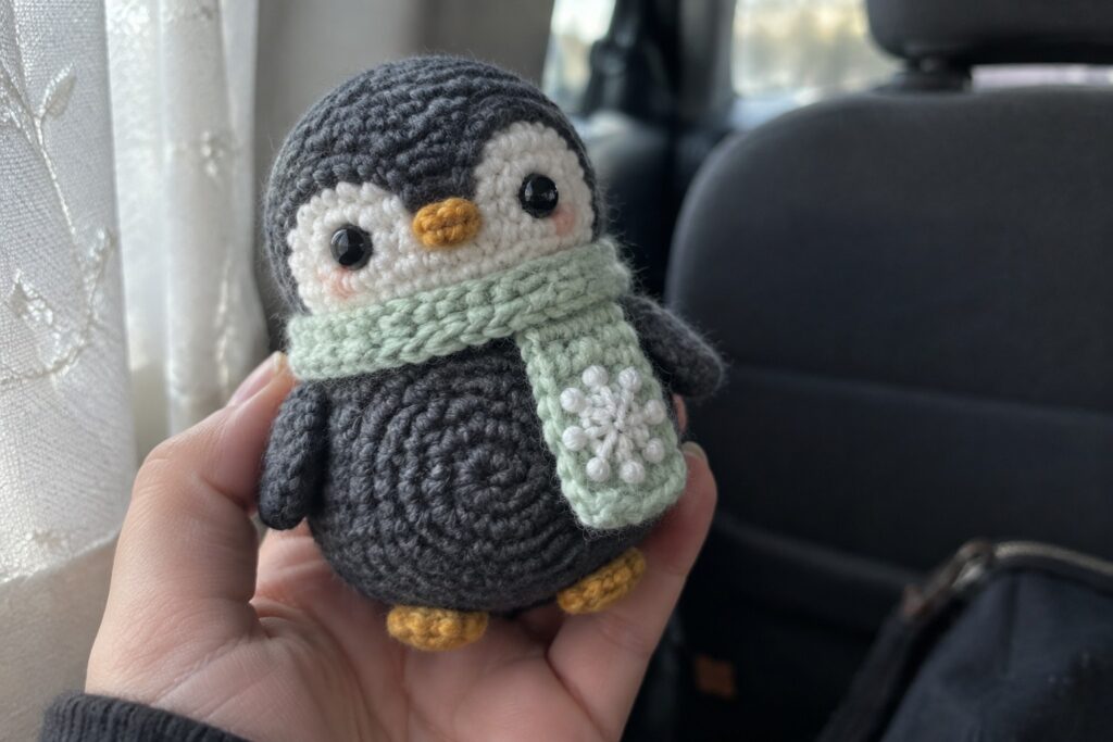 Hand holding crocheted gray penguin with light green snowflake scarf in car