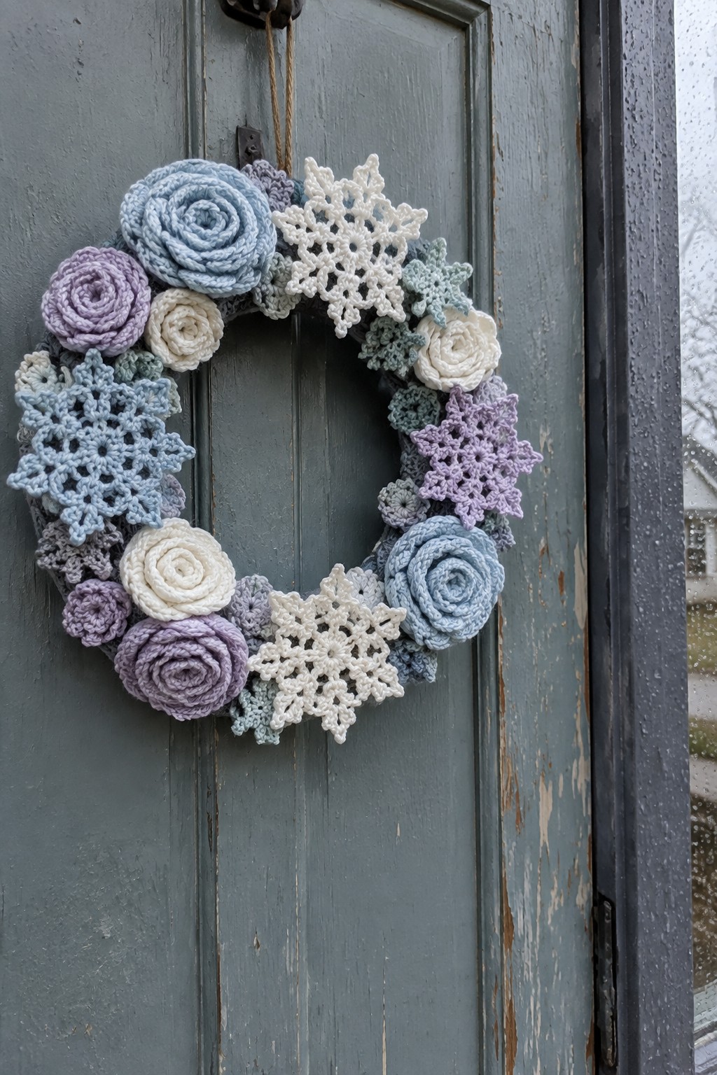 Crocheted wreath with pastel roses and snowflakes on weathered gray door