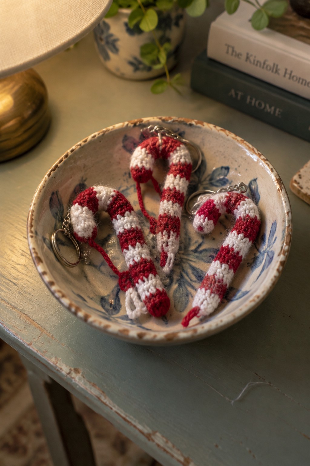 Three red and white crocheted candy cane keychains in a floral ceramic bowl