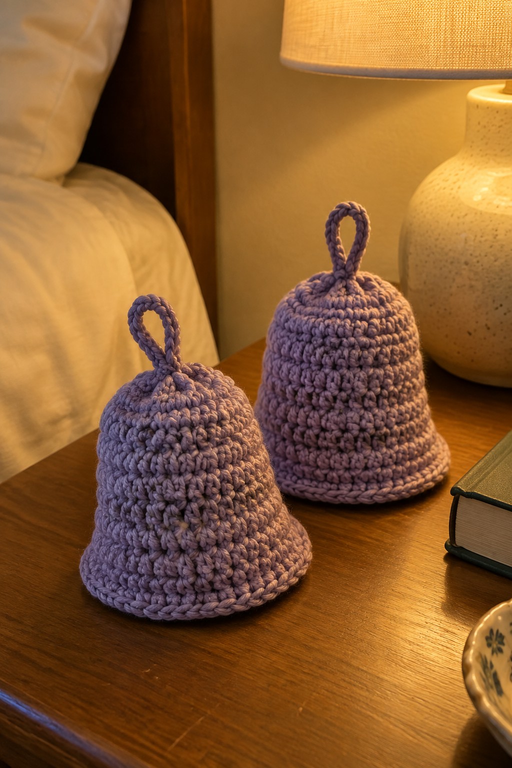 Two purple crocheted bells on a wooden nightstand beside a lamp