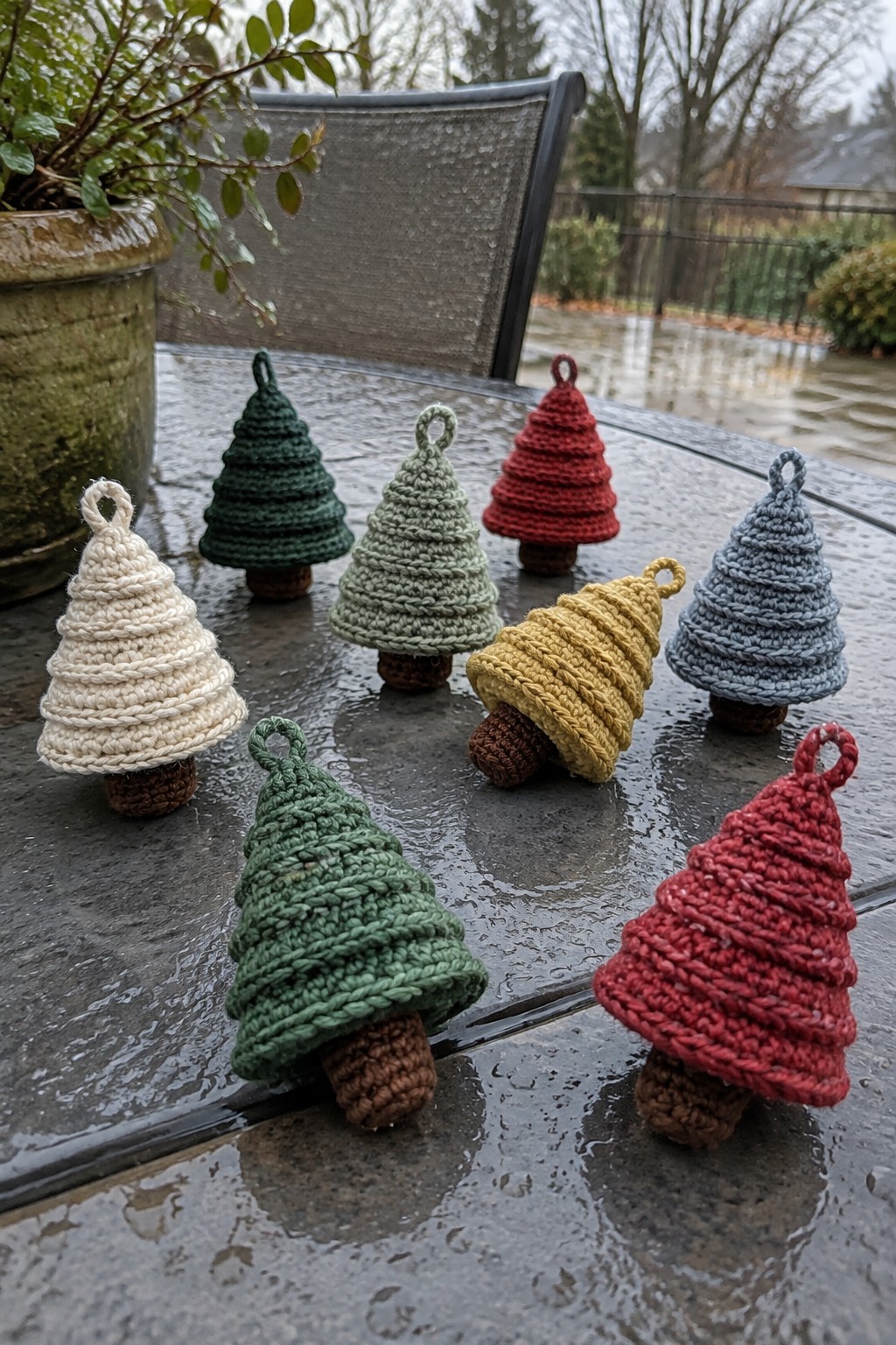 Colorful crocheted Christmas tree ornaments on a wet outdoor glass table