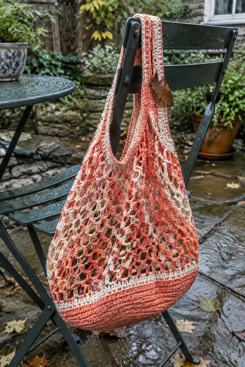Coral crocheted net bag draped over wet black metal chair on patio