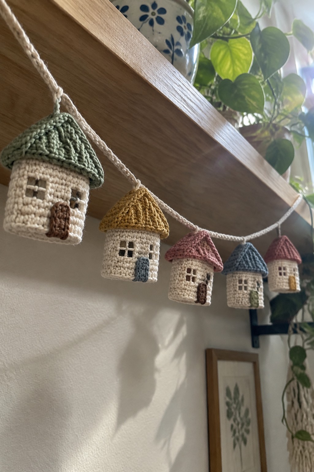 Crocheted miniature houses with colorful roofs hang from a cord under a shelf.