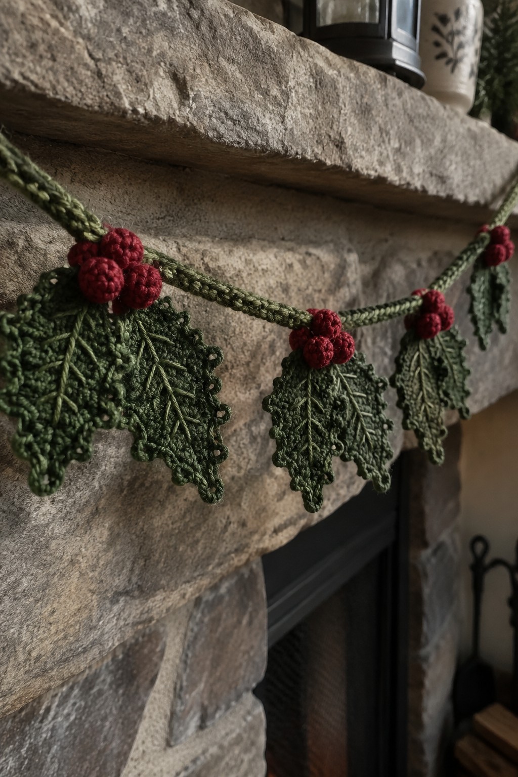Green crocheted holly garland with red berries on stone fireplace mantel