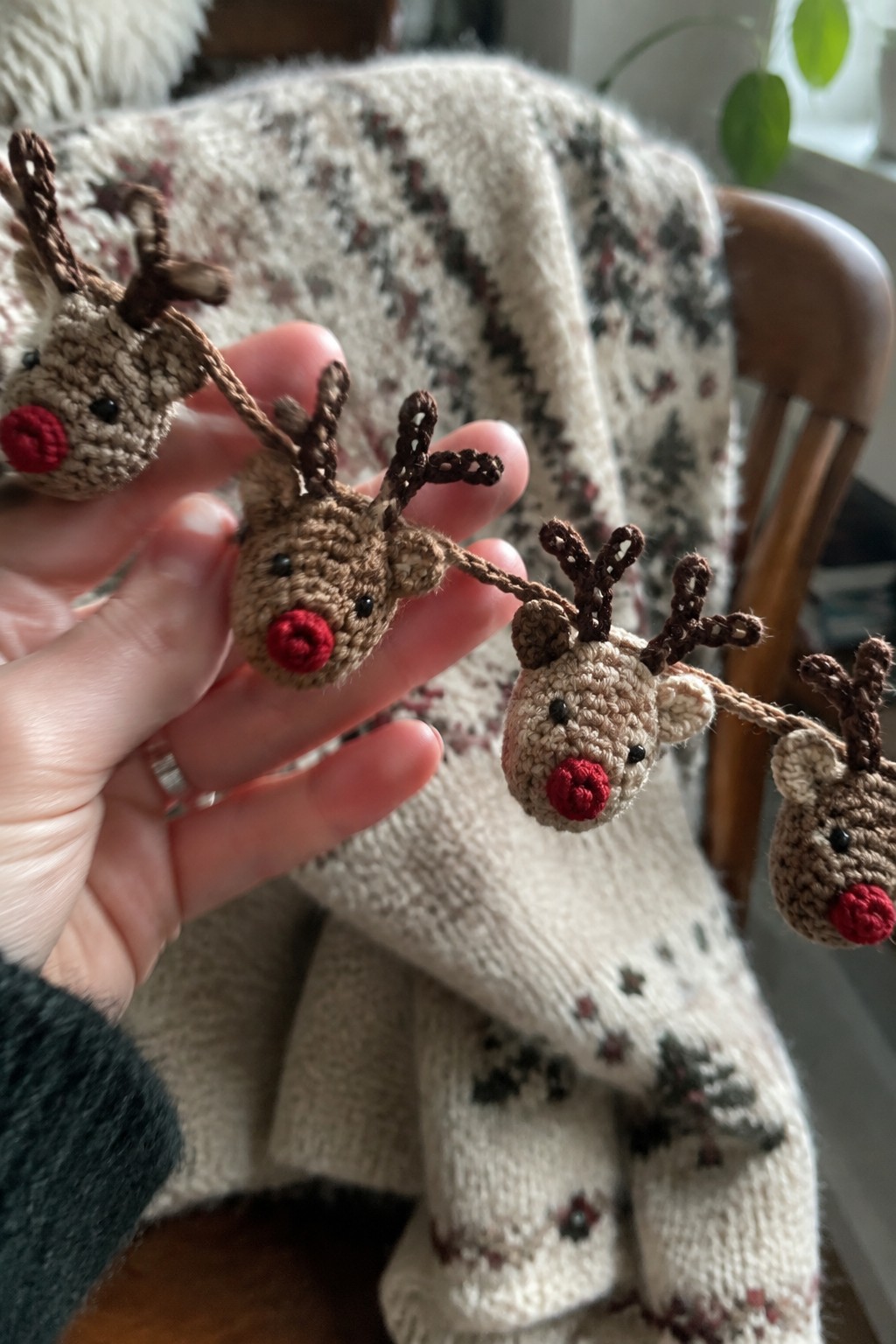 Hand holding crocheted reindeer garland with red noses over patterned knit blanket