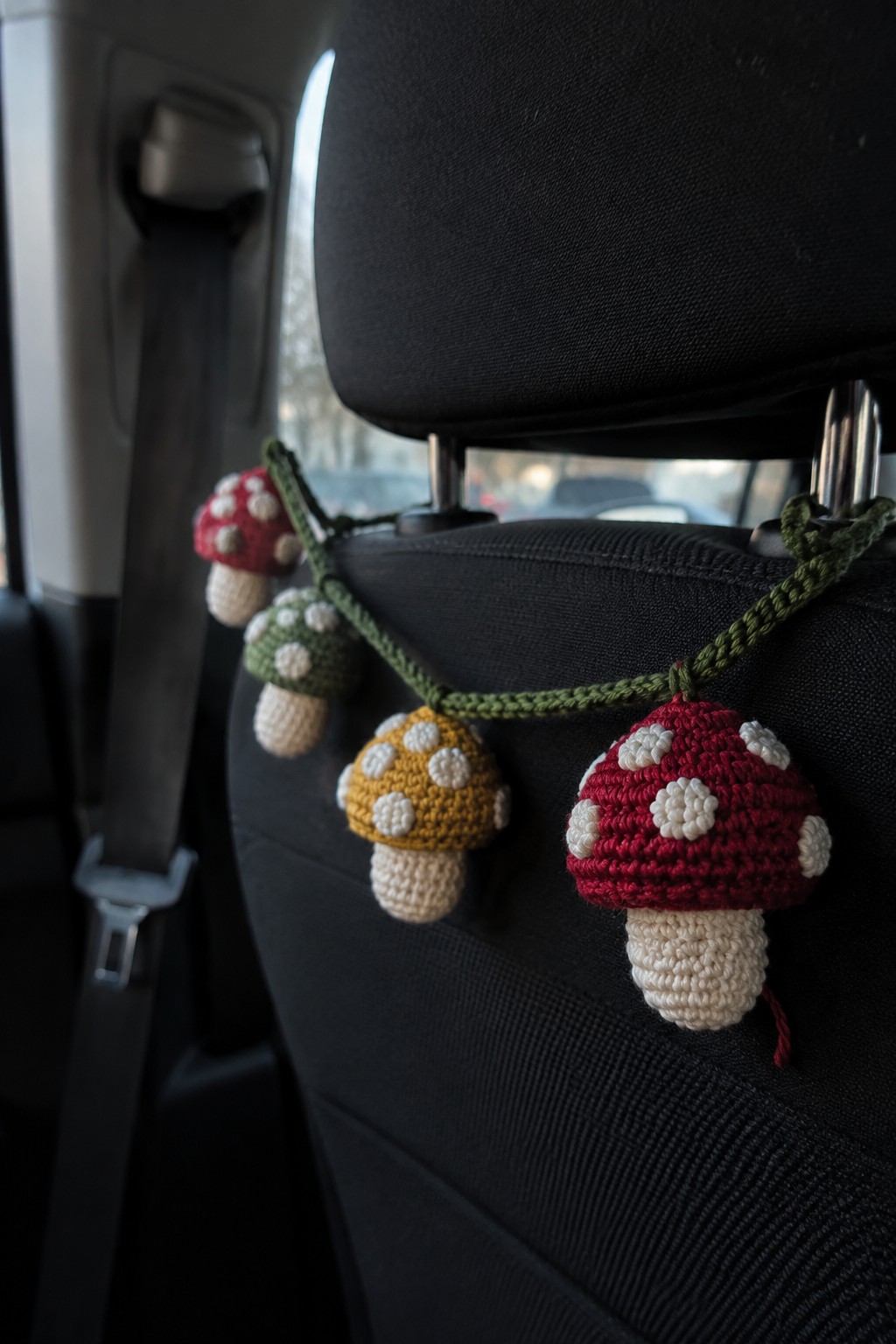 Crocheted red, yellow, and green mushrooms with white spots on car seat.
