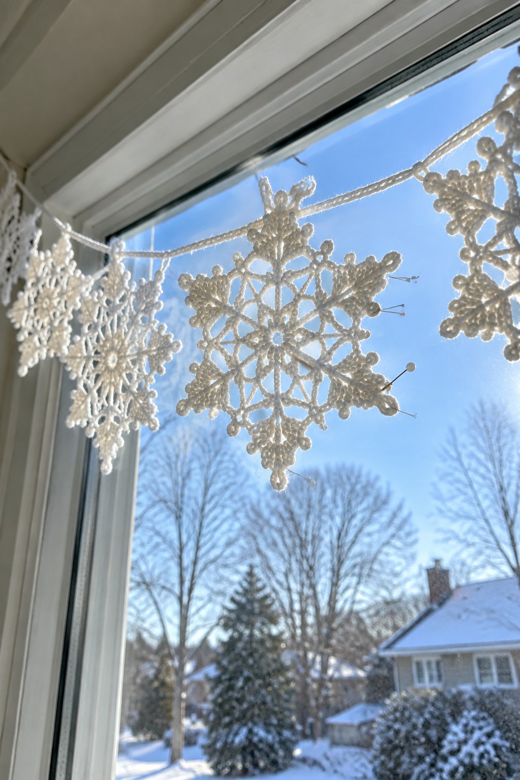 White crocheted snowflake garland strung across window with snowy landscape beyond