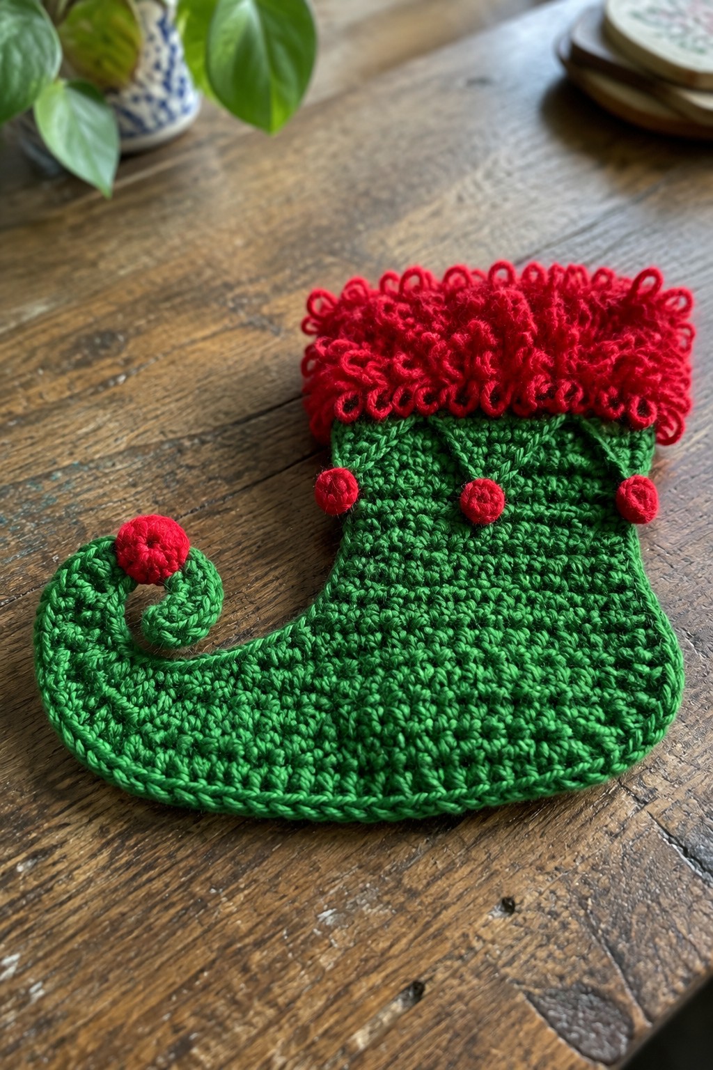 Green crocheted Christmas stocking with red ruffled cuff, pom-poms, and curled toe
