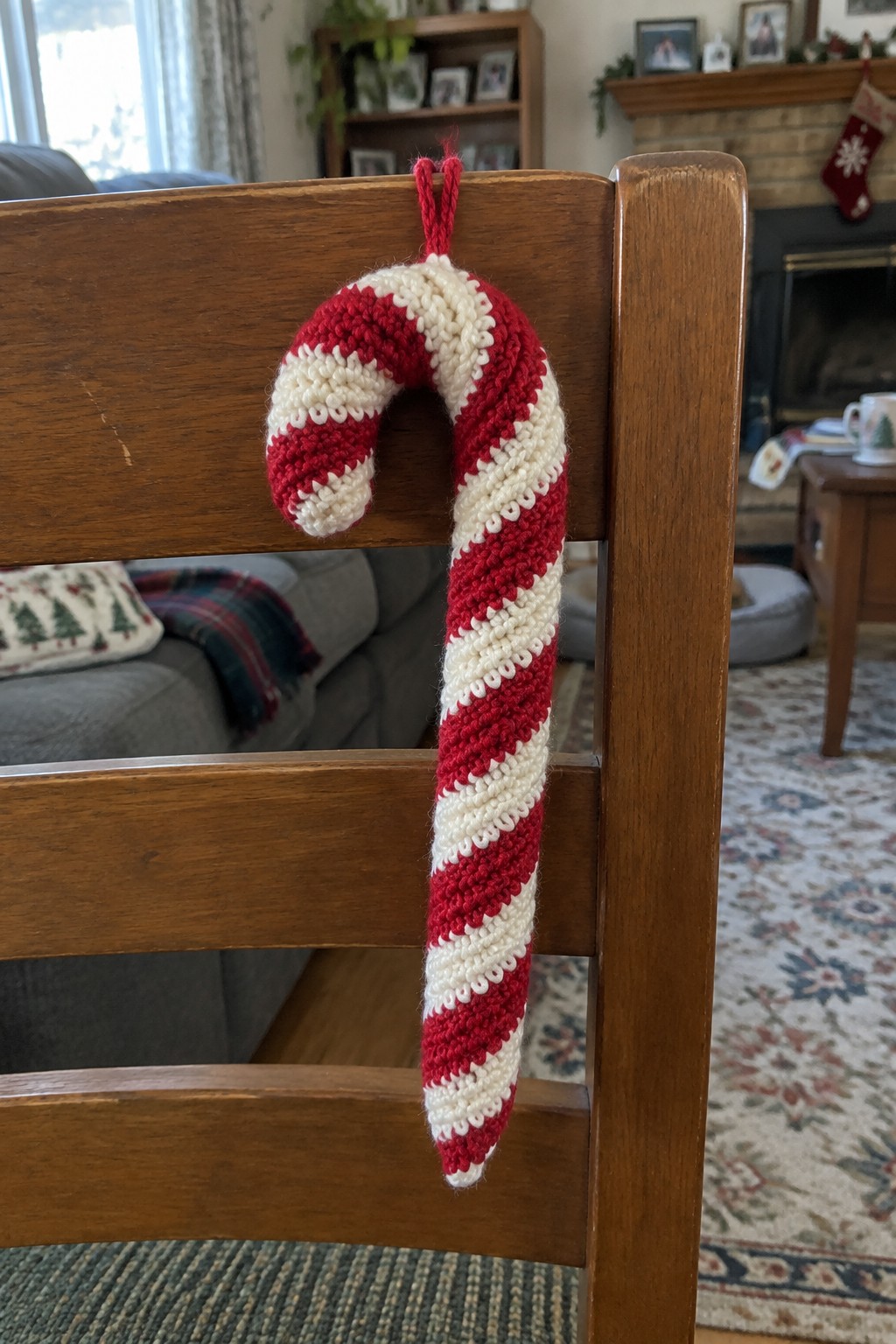 Red and white knitted candy cane ornament hanging on wooden chair back