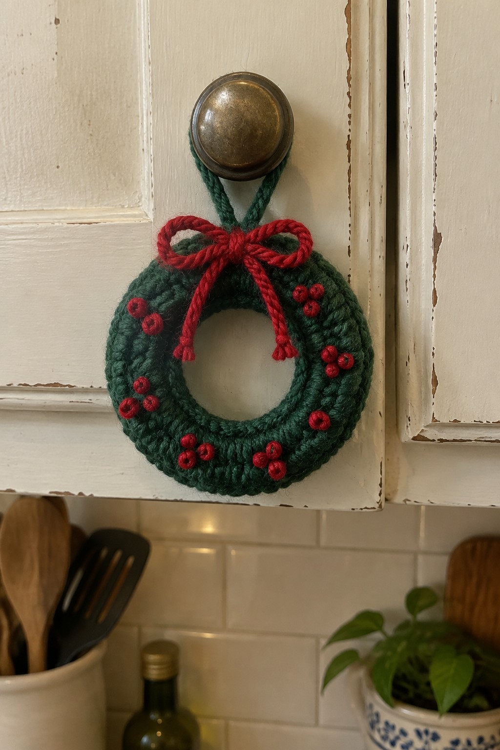 Crocheted green wreath with red bow and berries on white cabinet doorknob