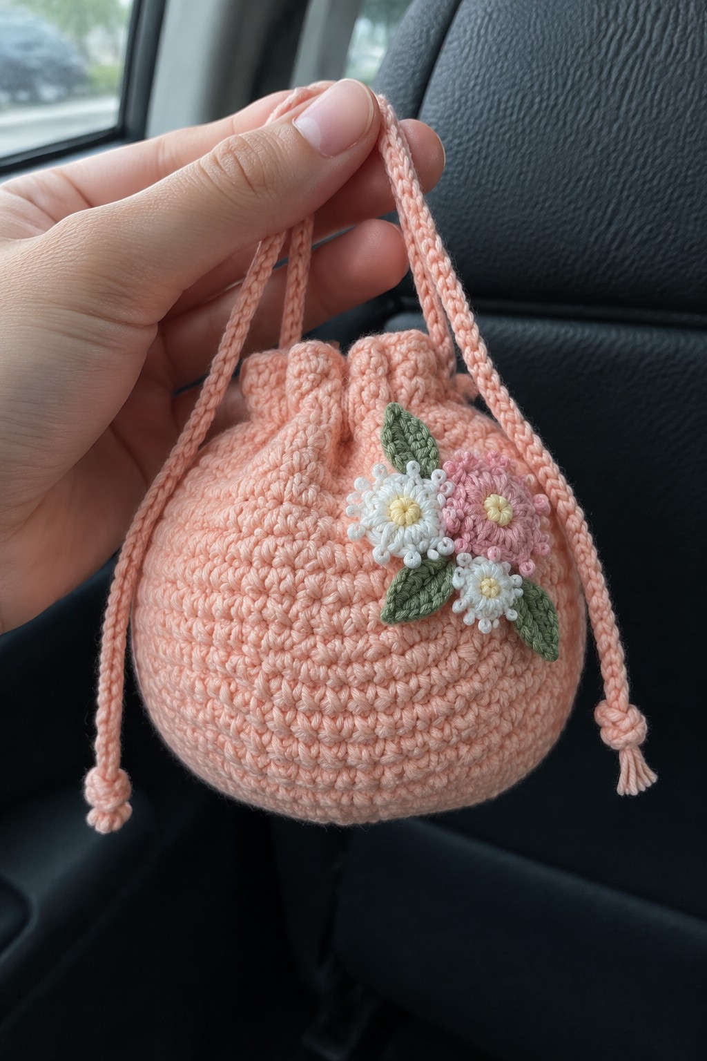 Hand holding peach crocheted drawstring pouch with white and pink flowers