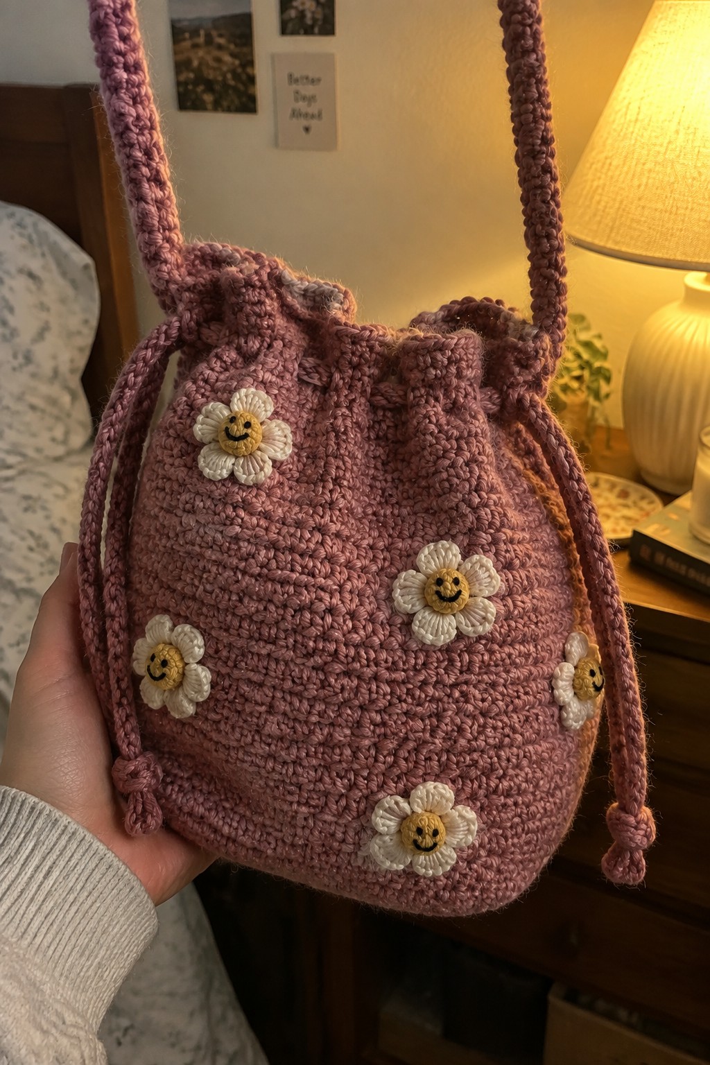 Hand holding pink crocheted drawstring bag with smiley face flowers