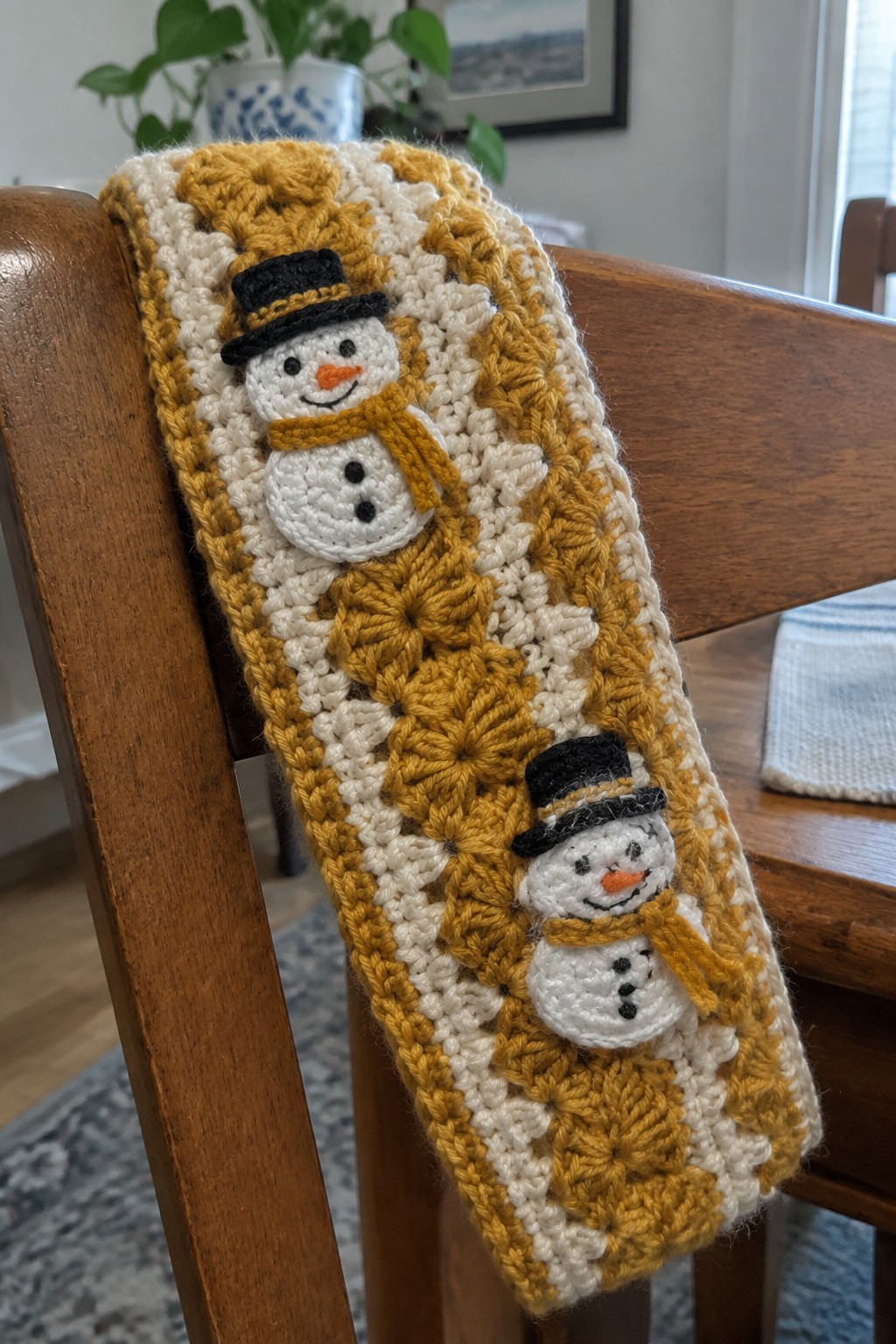 Yellow and cream crocheted scarf with two snowman appliques on wooden chair