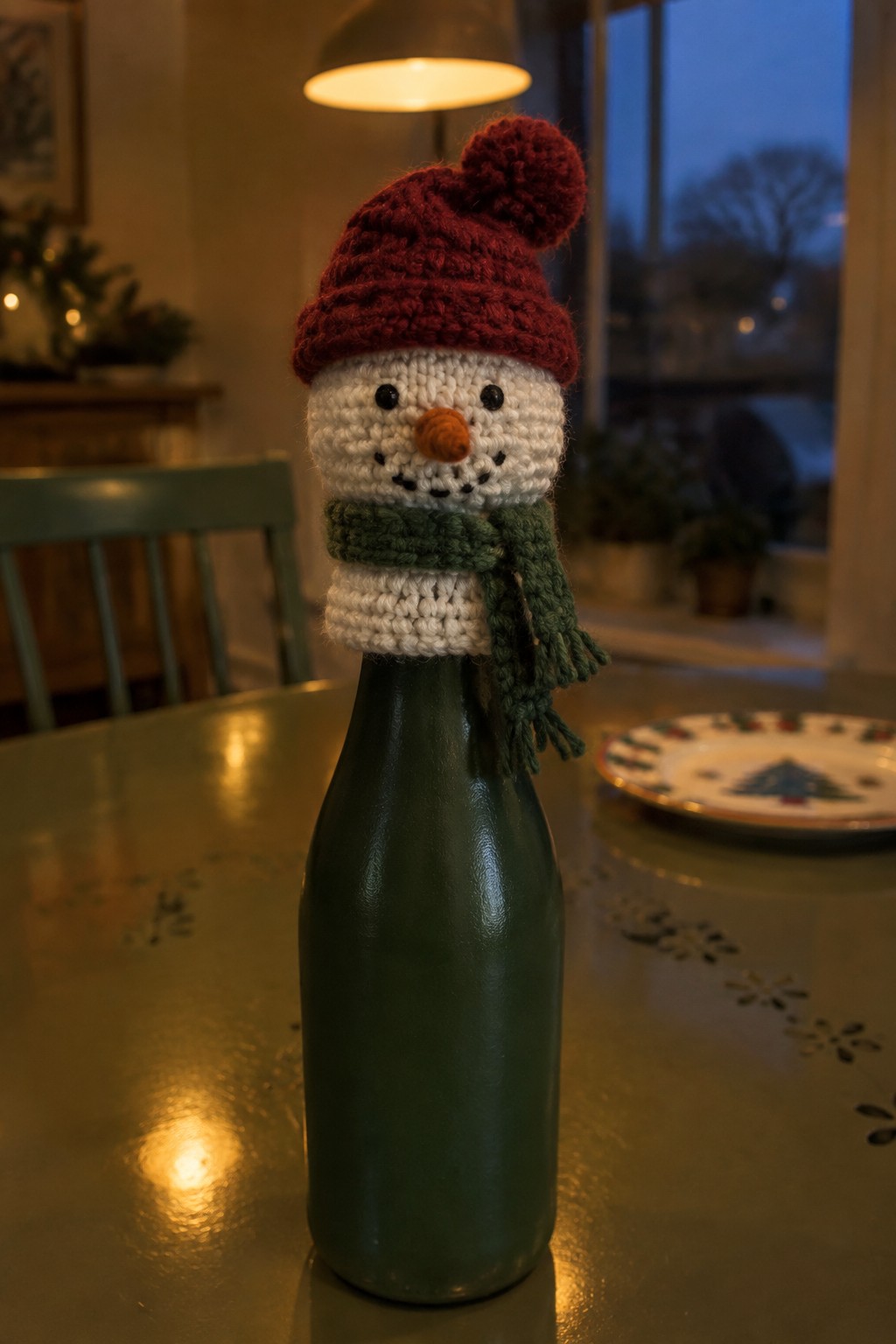 Crocheted snowman with red pom-pom hat and green scarf on green bottle.