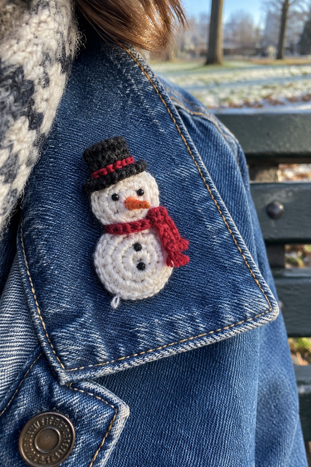 Crocheted snowman brooch with black hat and red scarf on blue denim jacket