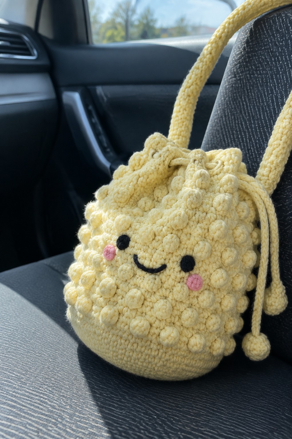 Yellow crocheted drawstring bag with smiling face on car seat.
