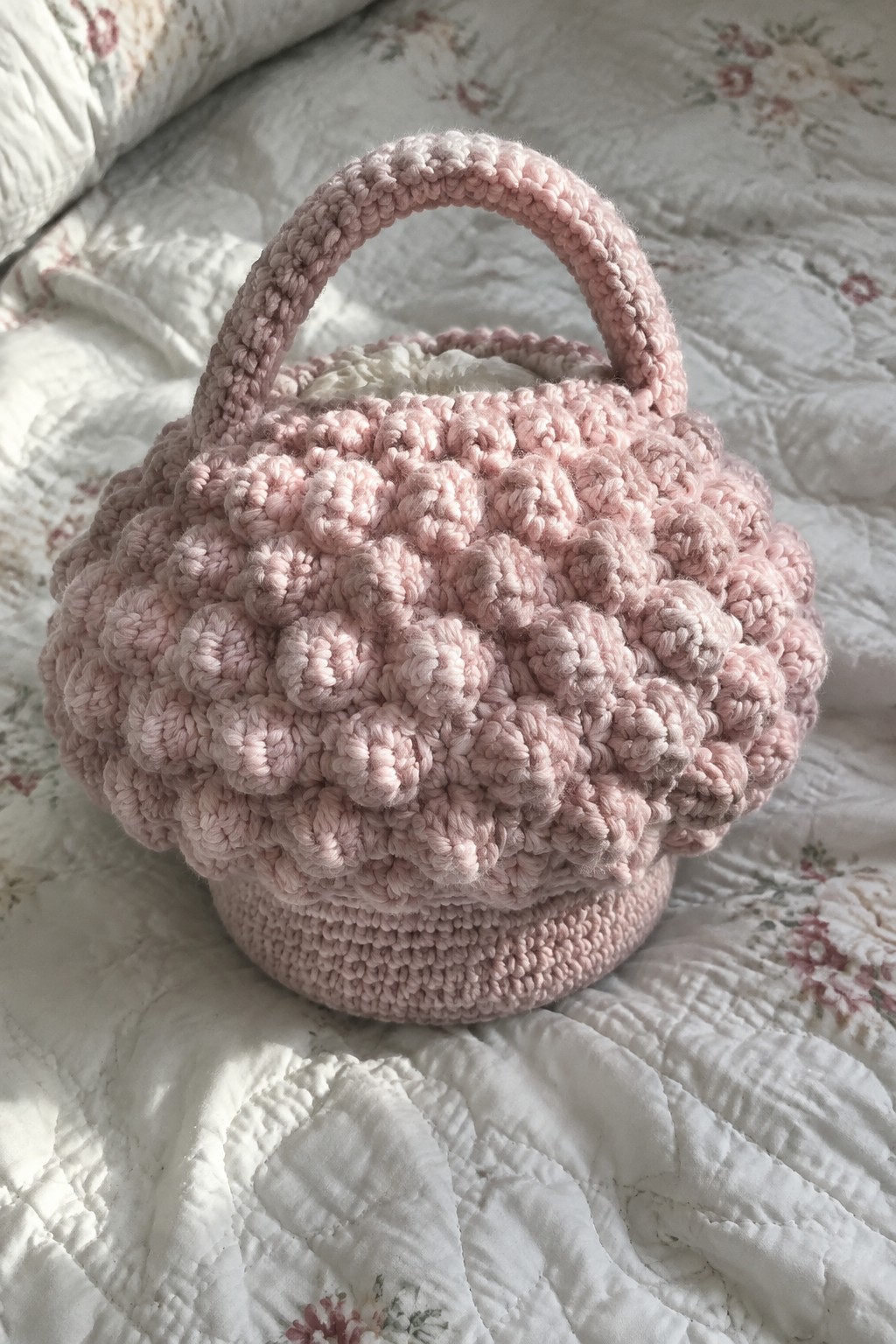 Pink crocheted basket with handle on floral quilted bedspread