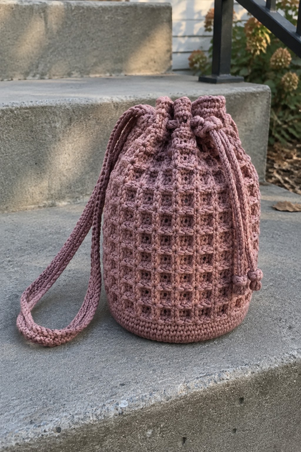 Dusty rose crocheted drawstring bucket bag on concrete outdoor steps