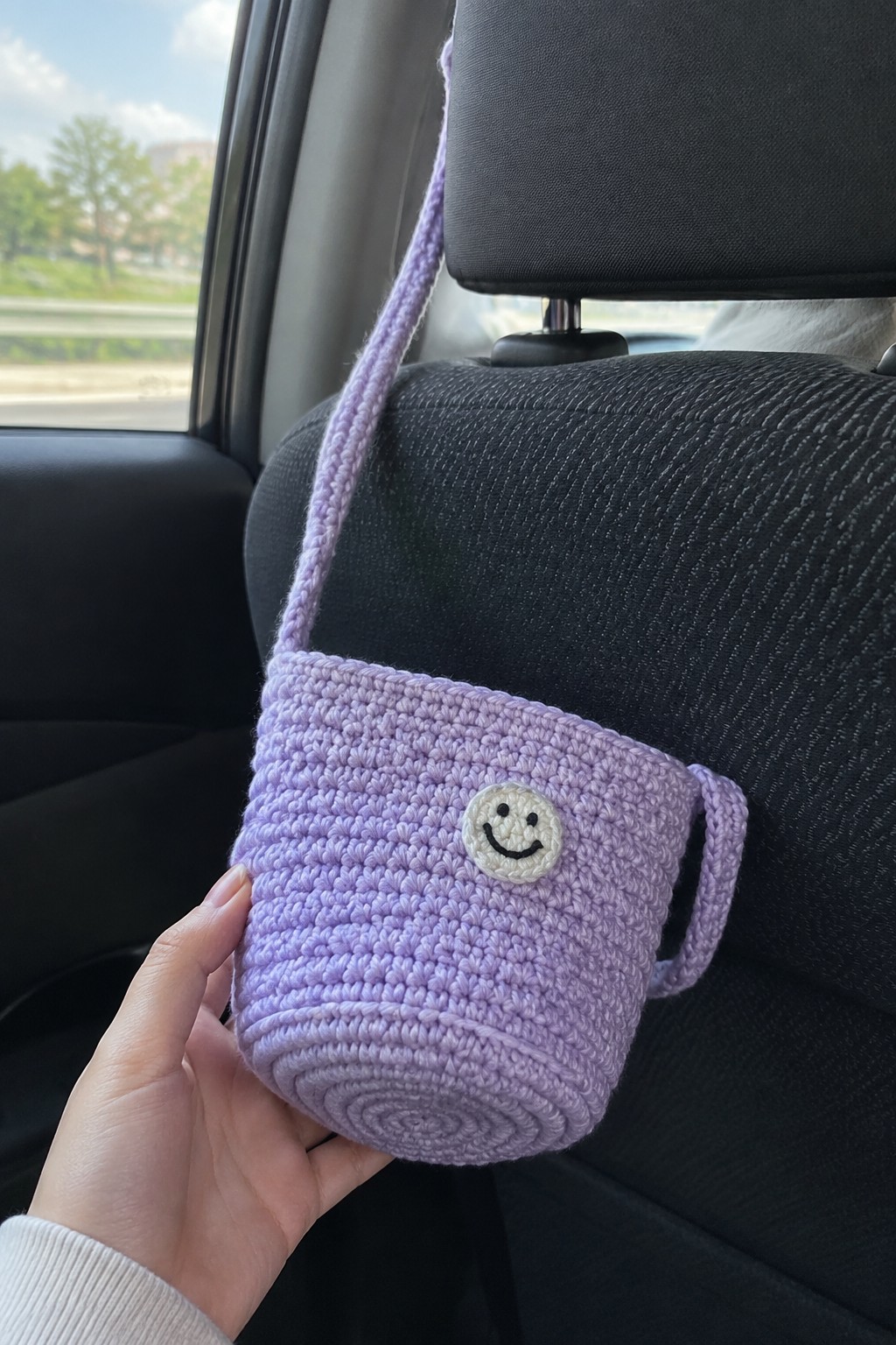 Hand holding purple crocheted pouch with smiley patch in car seat