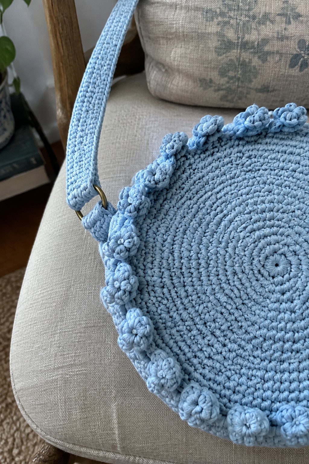 Light blue crocheted round bag with floral trim on beige chair