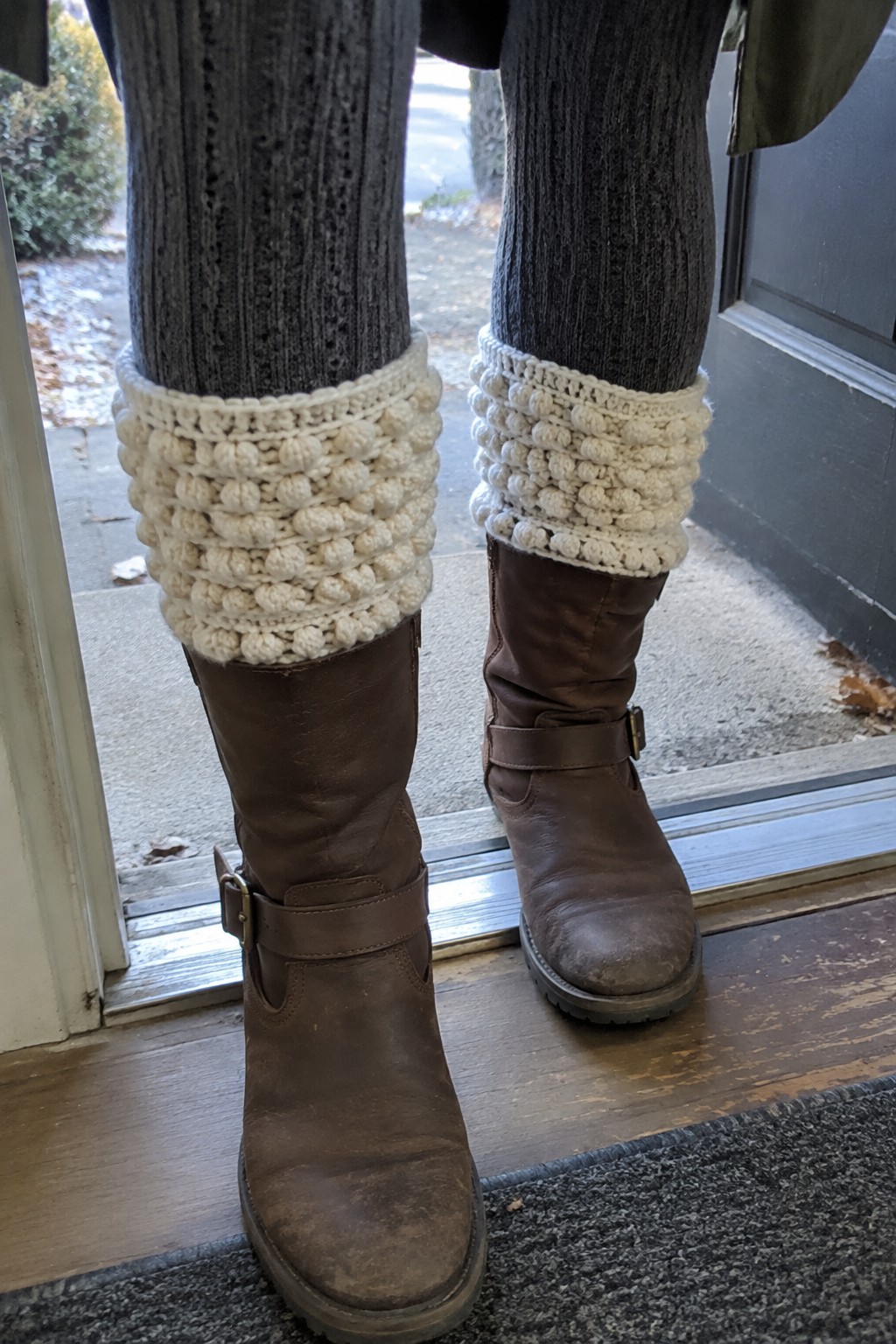 Brown leather boots with white bobble-knit cuffs over gray ribbed socks at doorway.
