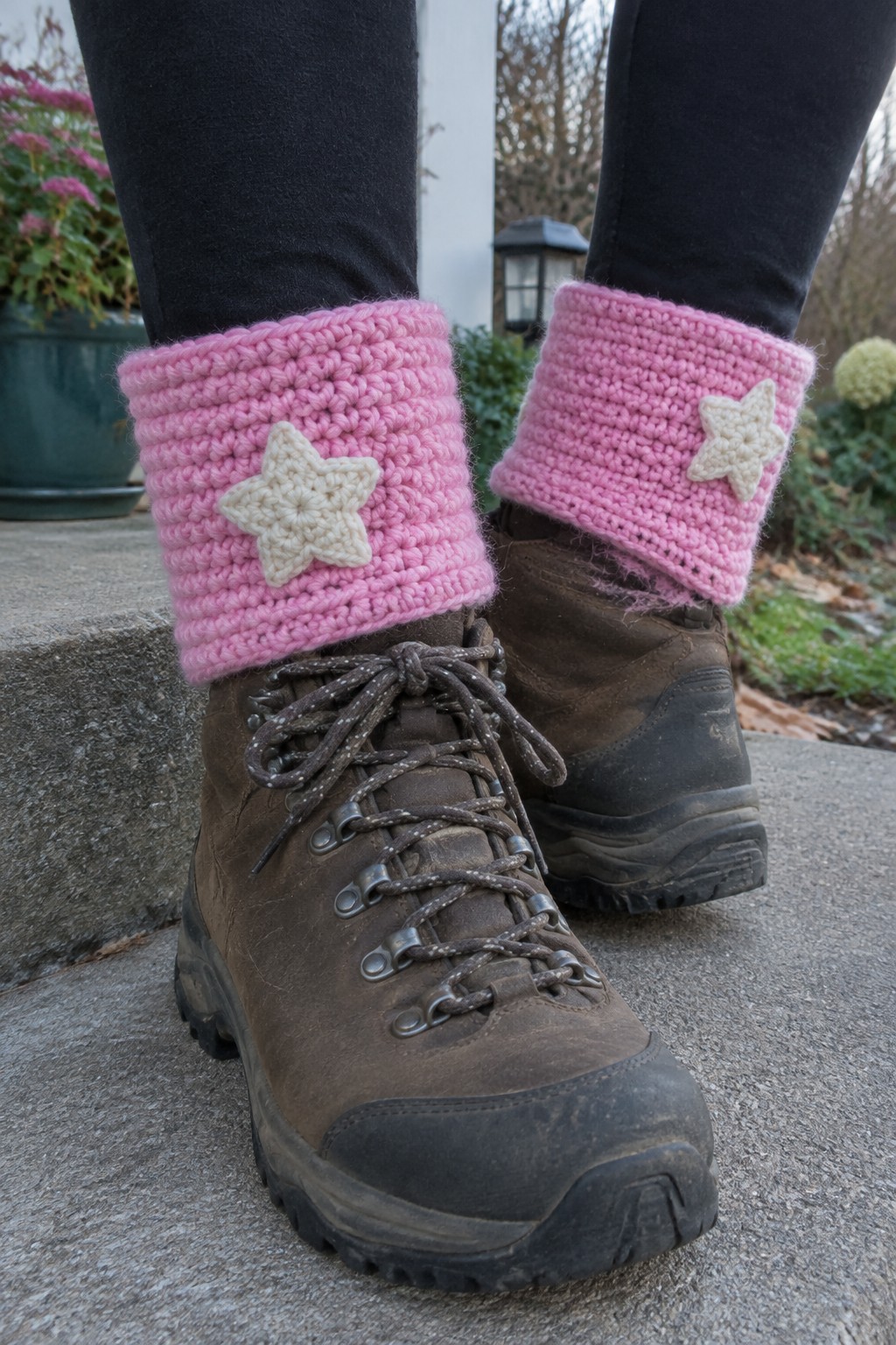 Brown hiking boots with rolled pink crocheted cuffs and cream star appliques, shown over black leggings on stone steps.