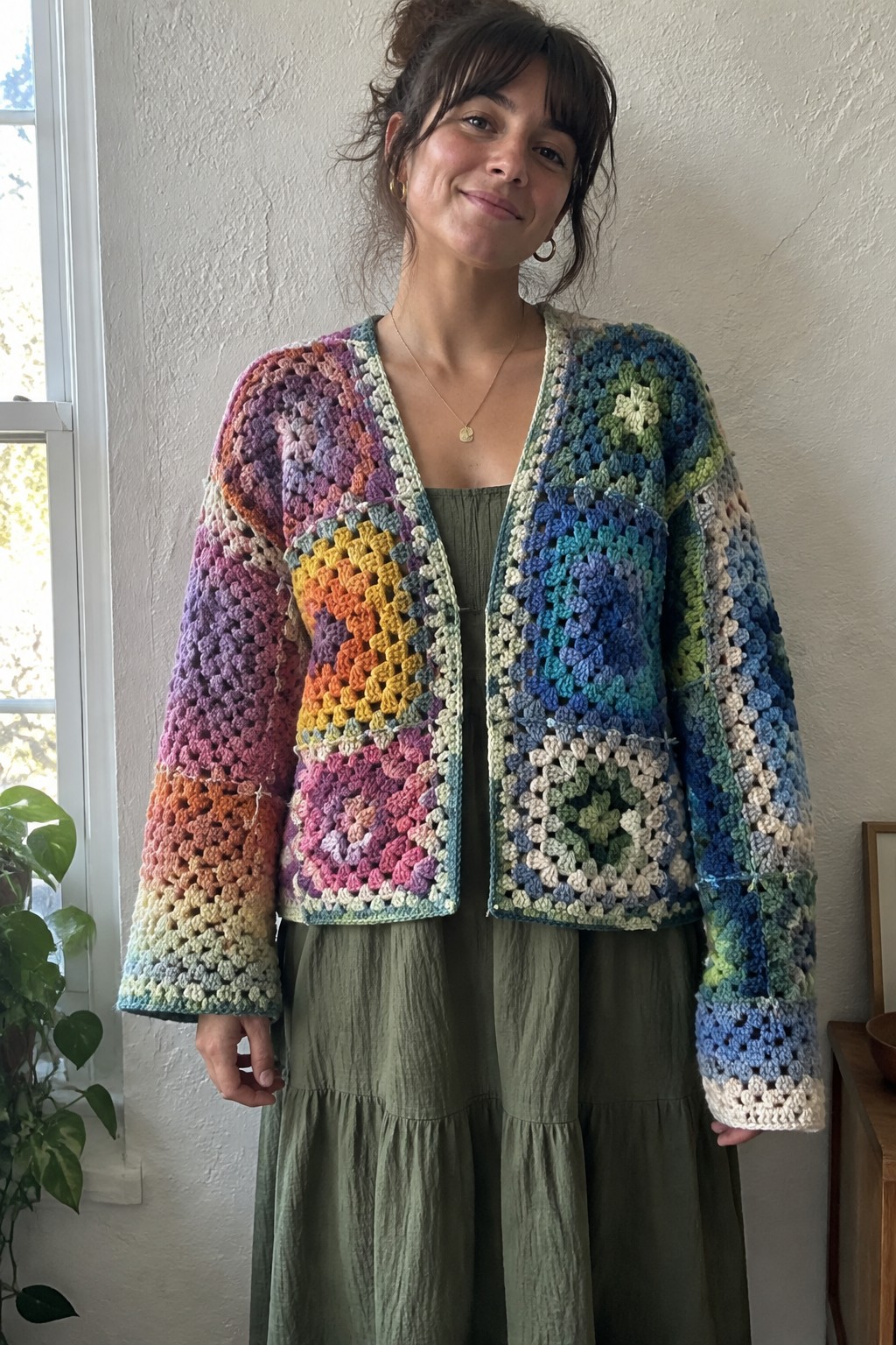 Woman in vibrant multicolored granny square crocheted cardigan over green tiered dress