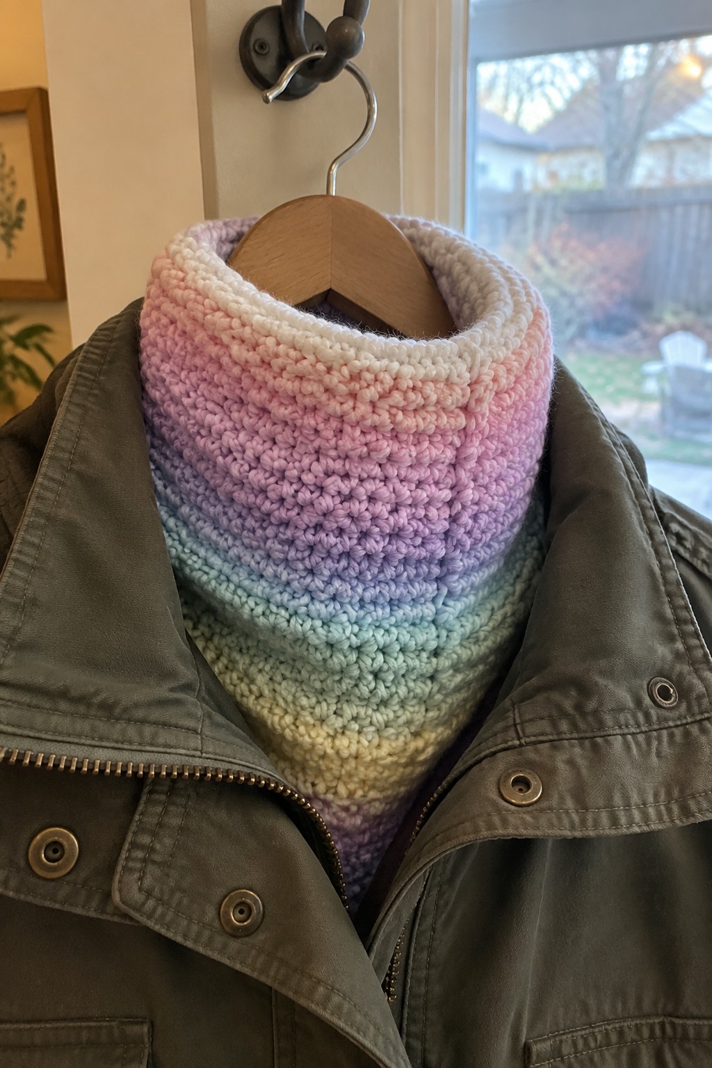 Chunky rainbow knit cowl draped over olive green jacket on wooden hanger