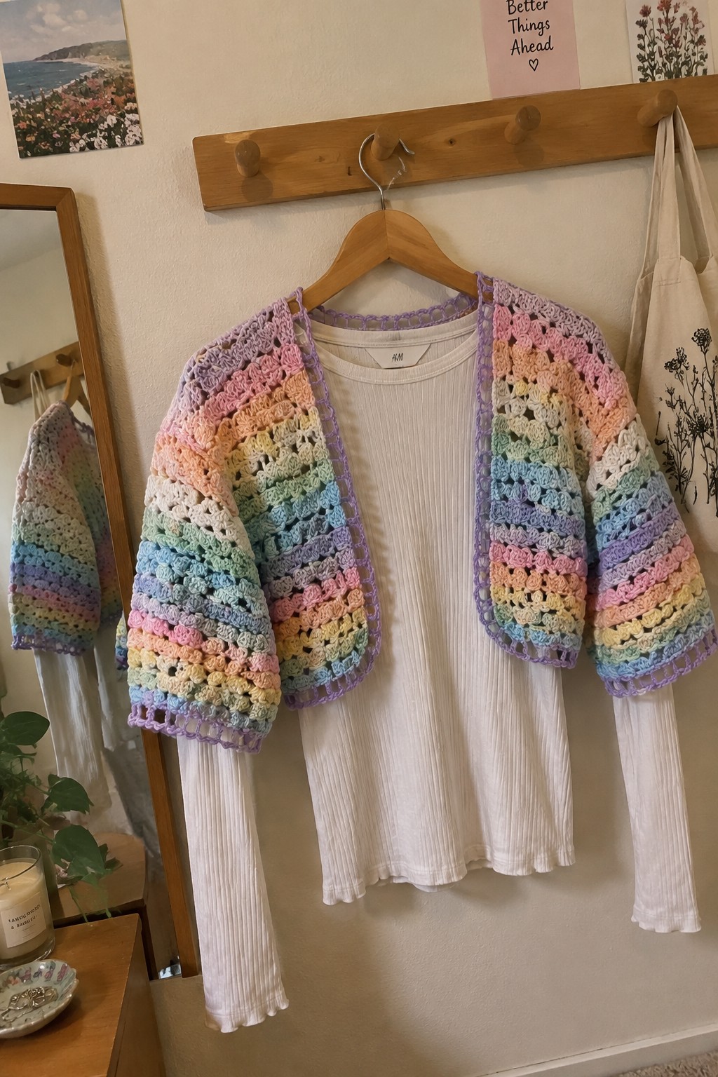 Rainbow crocheted cardigan on wooden hanger over white ribbed top