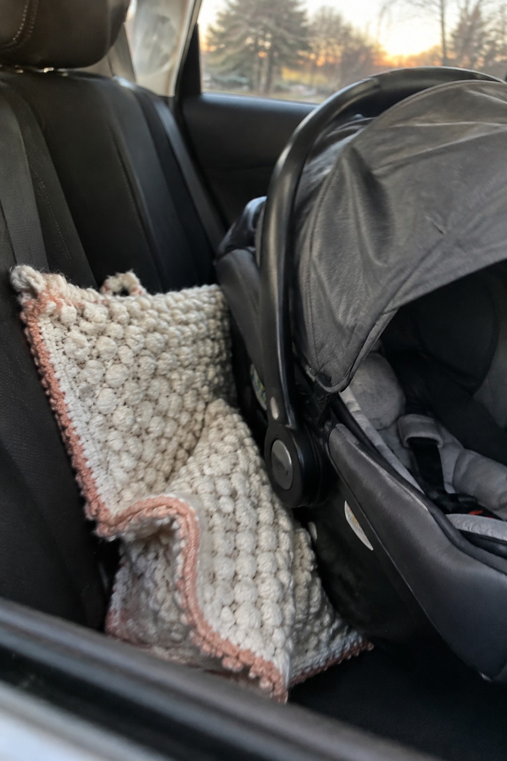 Knitted white blanket with pink trim beside gray infant car seat in vehicle
