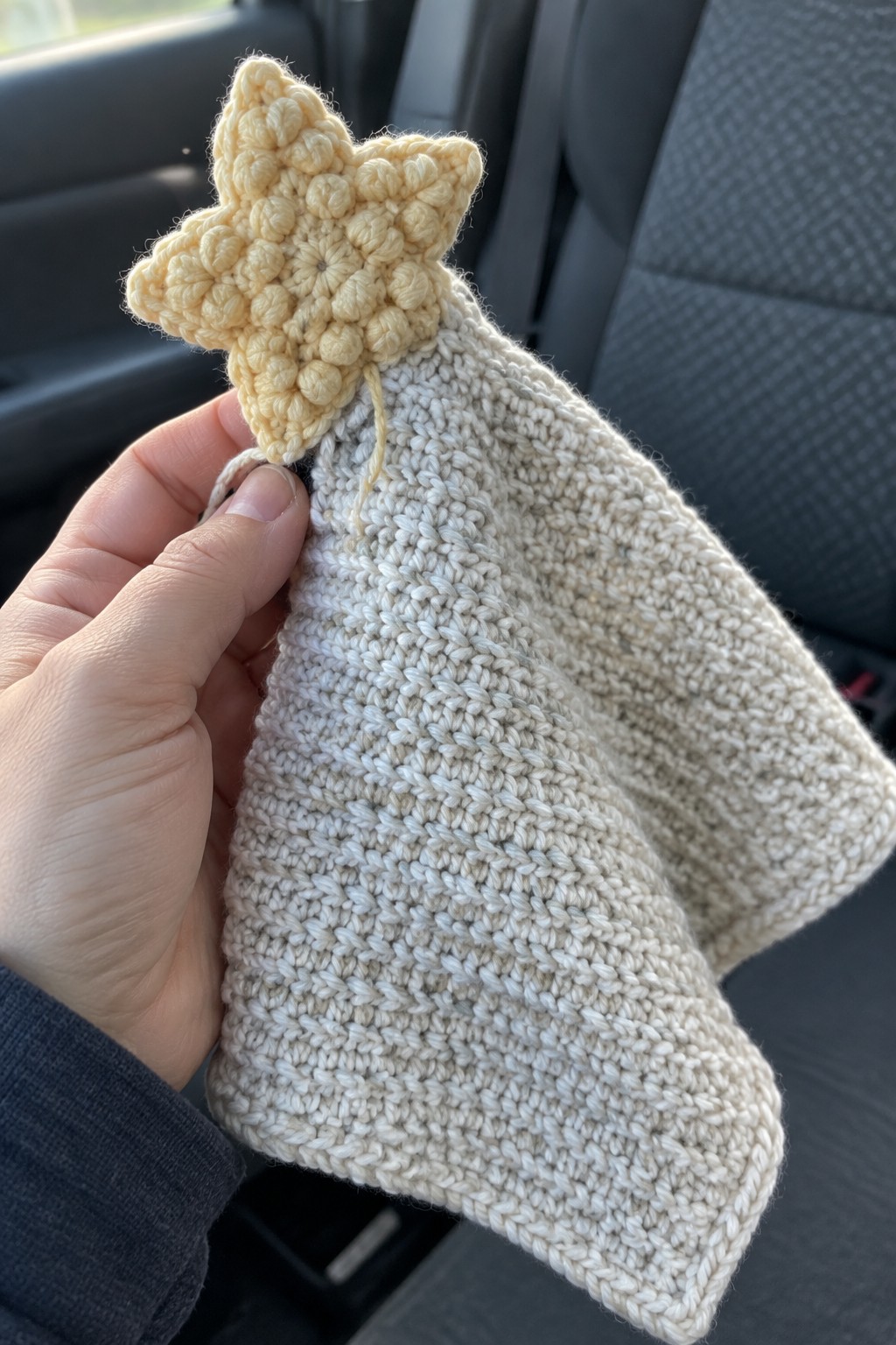 Hand holding beige crocheted lovey with yellow star inside a car