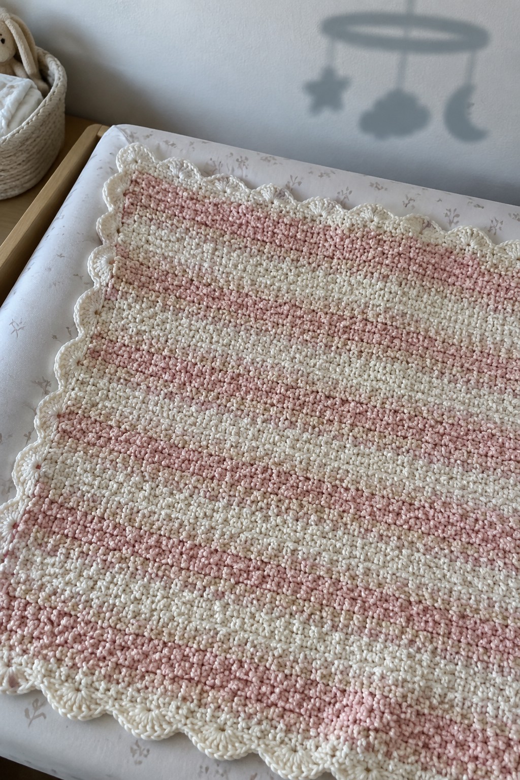 Pink and white striped crocheted blanket with scalloped edges on floral bedding.