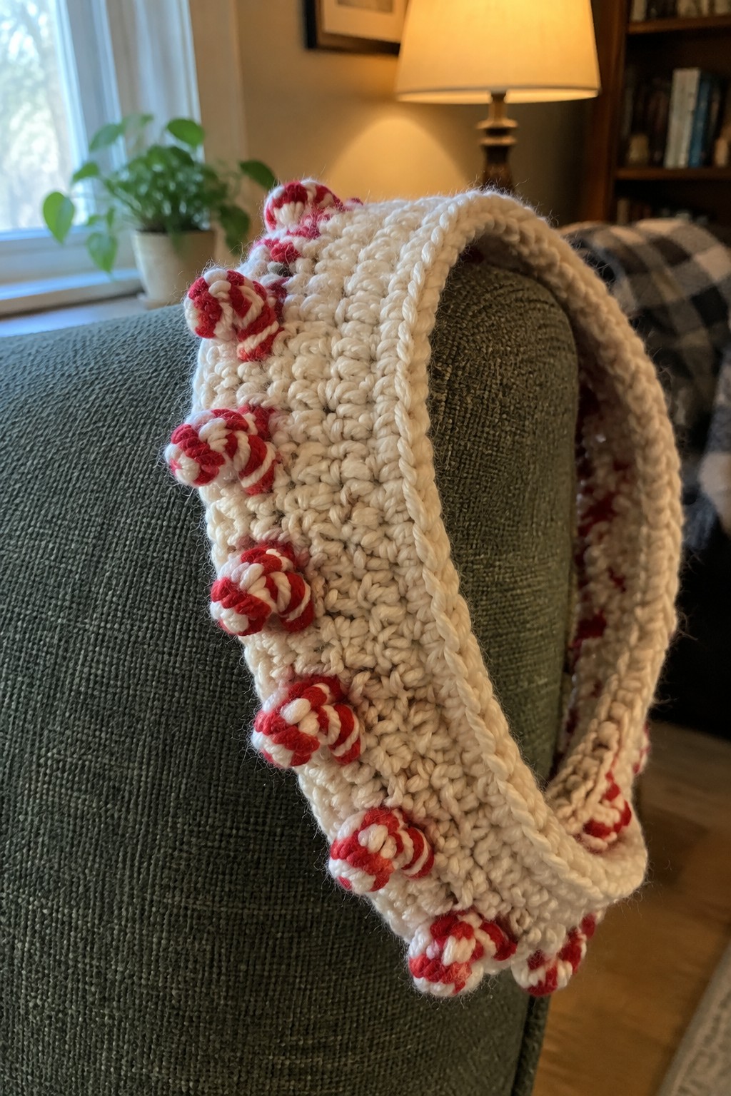 Chunky white knit headband with red striped pom-poms on green couch