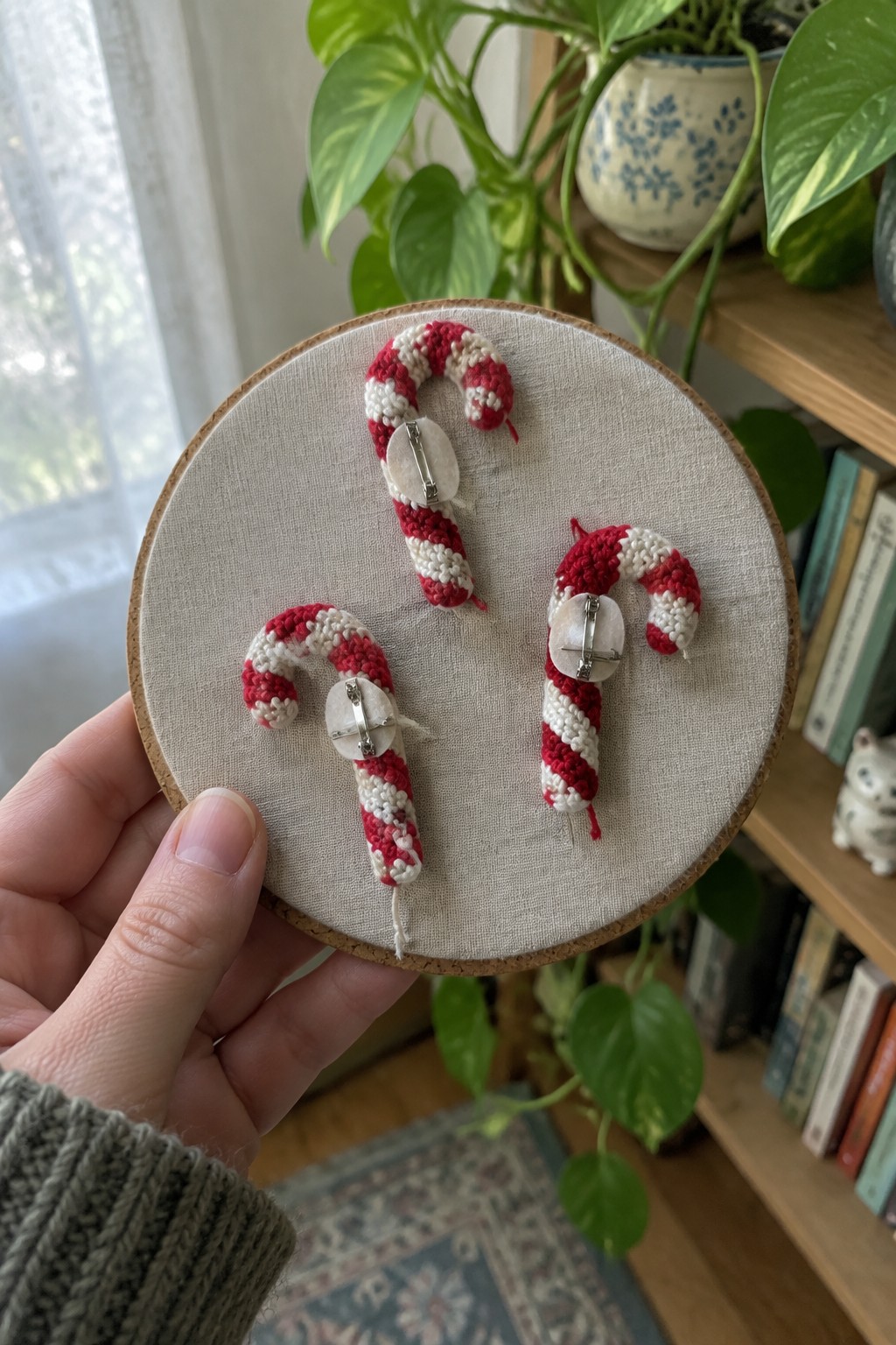 Hand holds embroidery hoop with three red and white crocheted candy cane pins