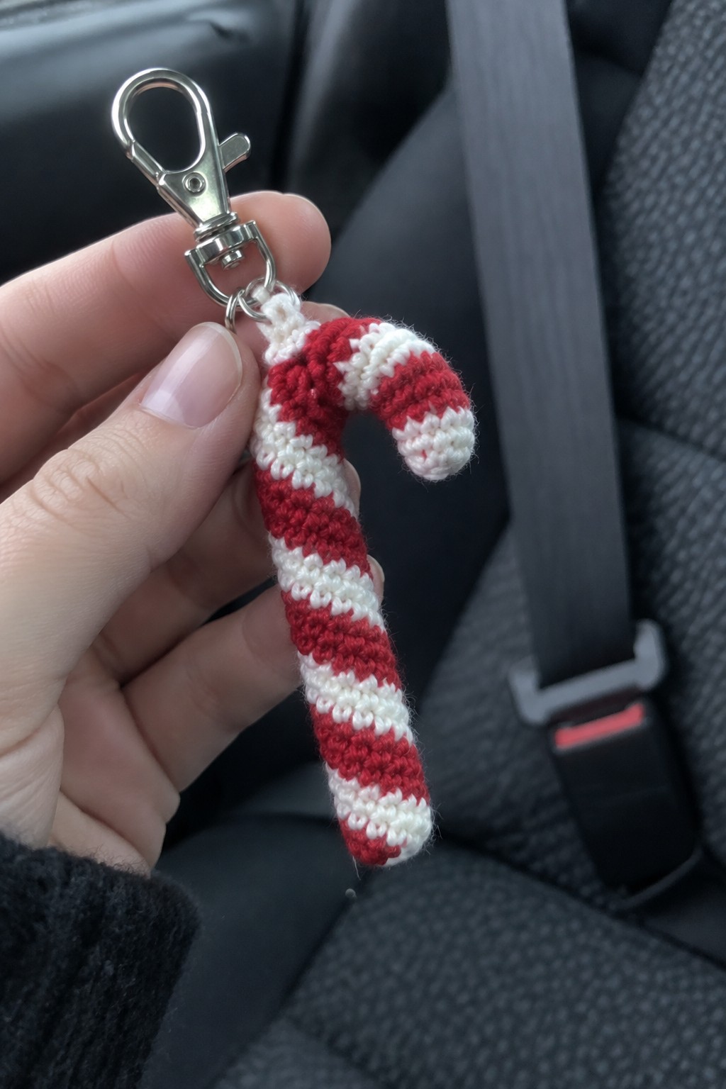 Hand holding crocheted red and white striped candy cane keychain with metal clasp in car