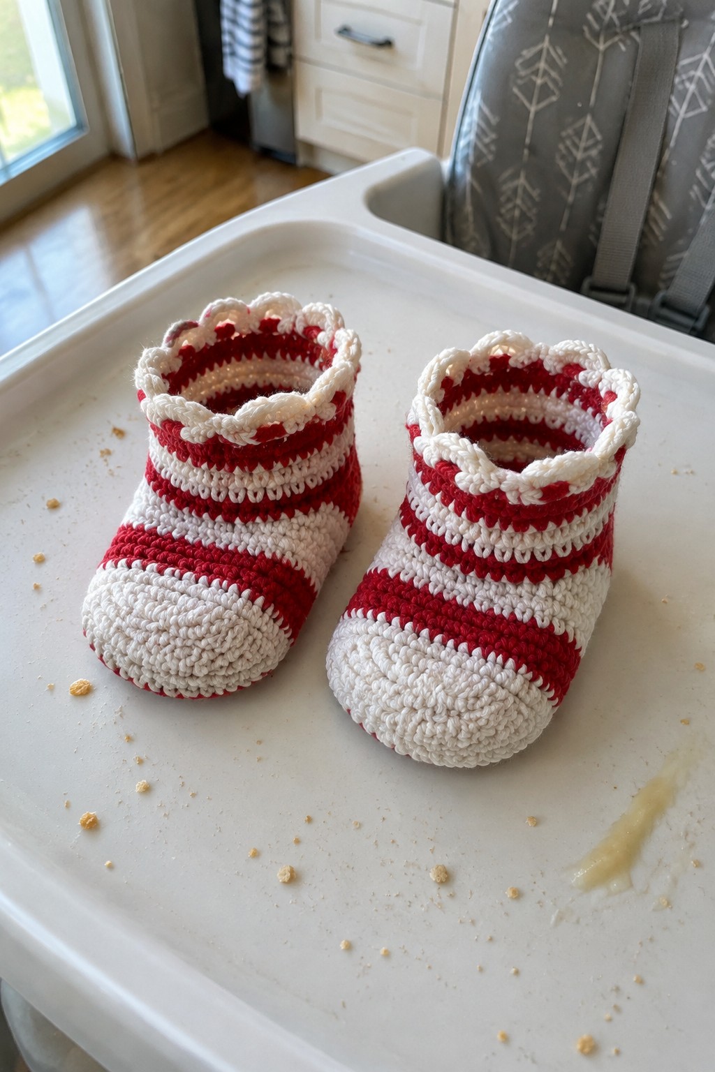 Red and white striped crocheted baby booties on white high chair tray.