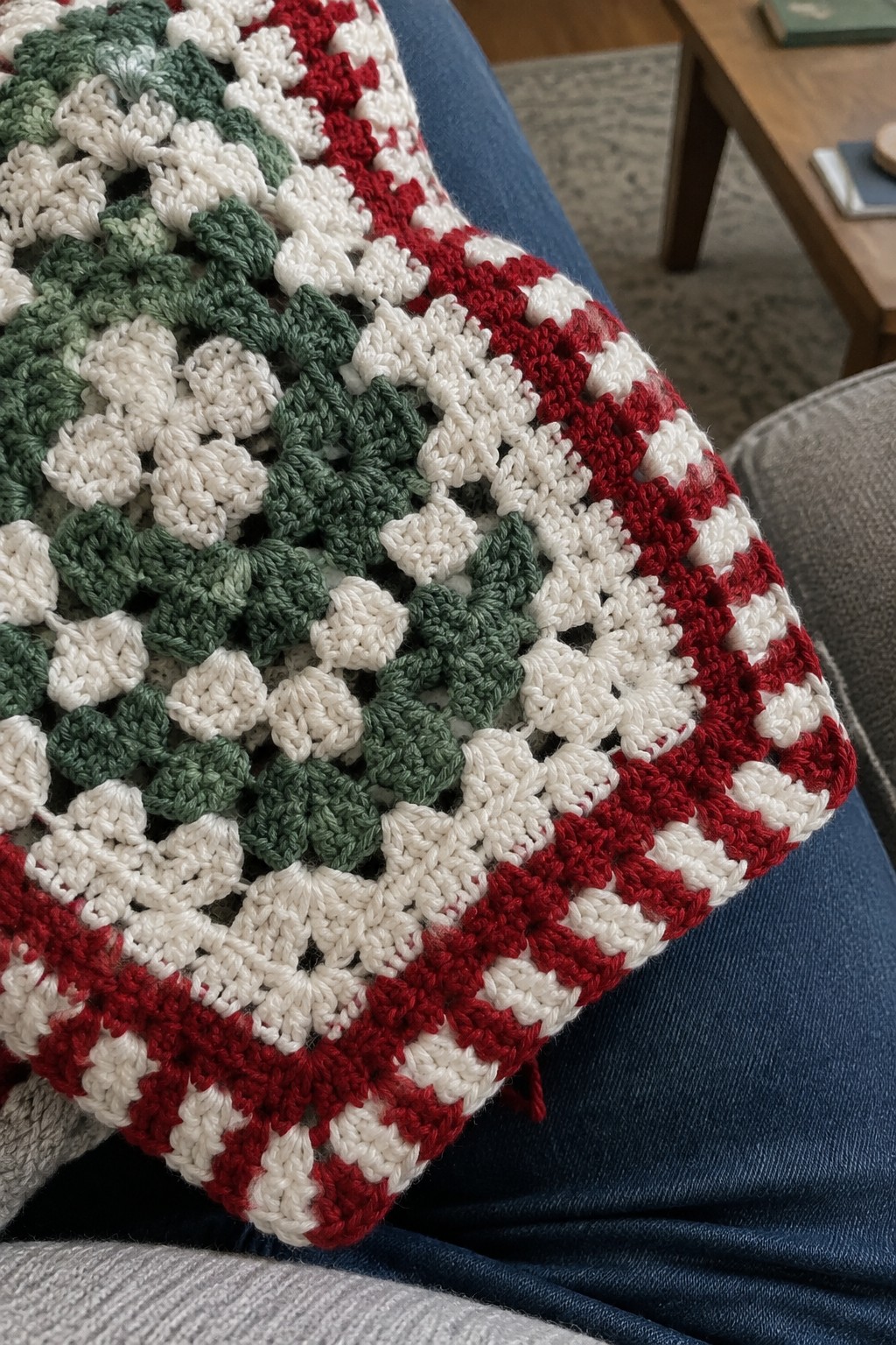 Crocheted red, white, and green granny square blanket draped over blue jeans.