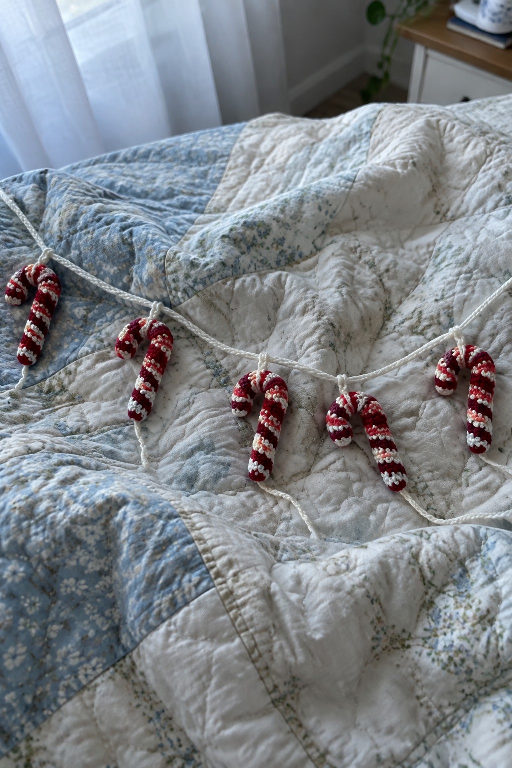 Crocheted red white pink candy cane garland on blue floral quilt