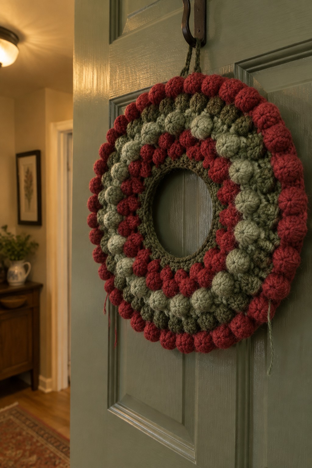Crocheted pom-pom wreath in red, green, and gray on a green door.