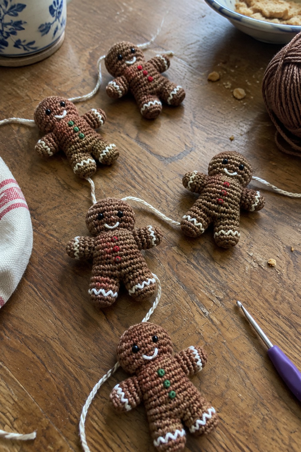 Crocheted gingerbread men with colorful buttons strung on yarn atop wooden table with hook