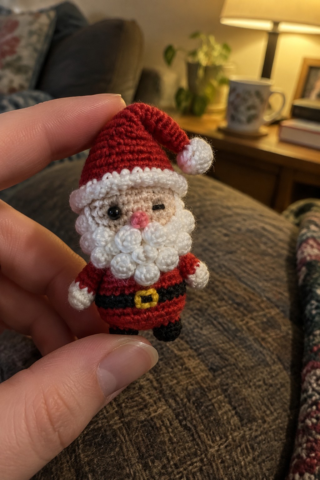 Fingers hold tiny crocheted Santa doll in red suit with white beard.