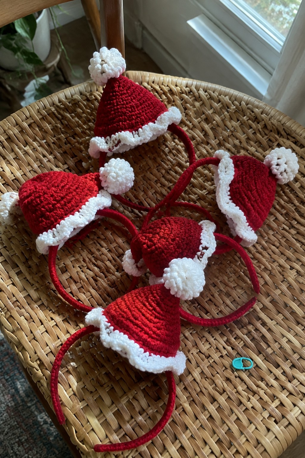 Crocheted Santa hats with pom-poms on red headbands atop a wicker chair