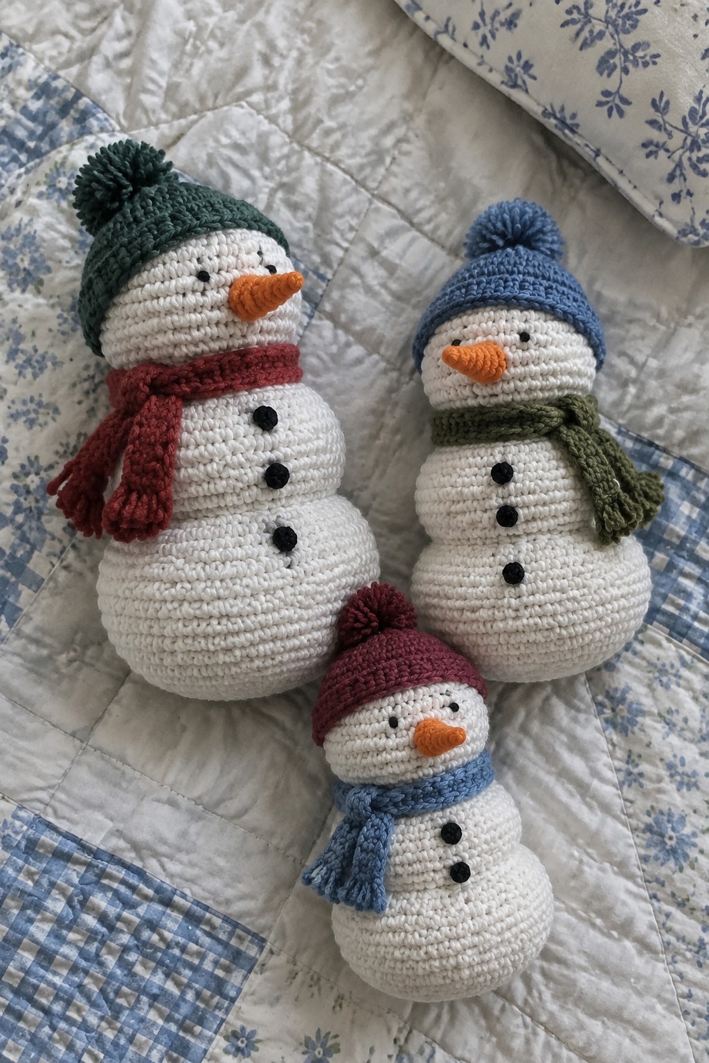 Three crocheted snowmen with pom-pom hats and scarves on a floral quilt