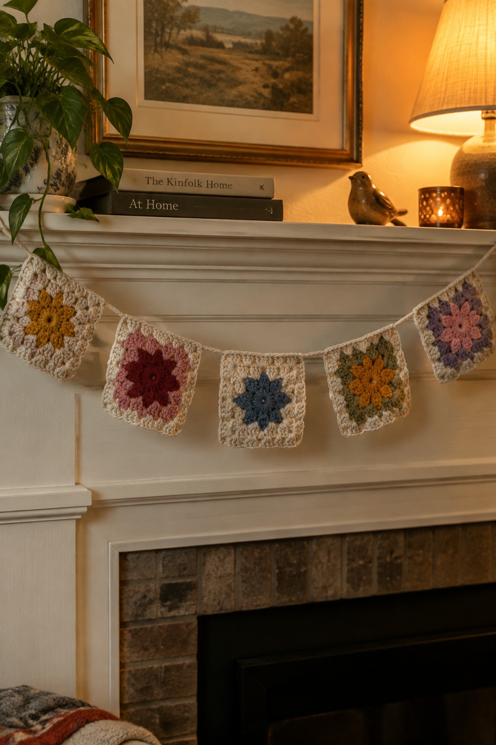 Colorful crocheted floral granny squares strung as garland on white fireplace mantel with books and lamp