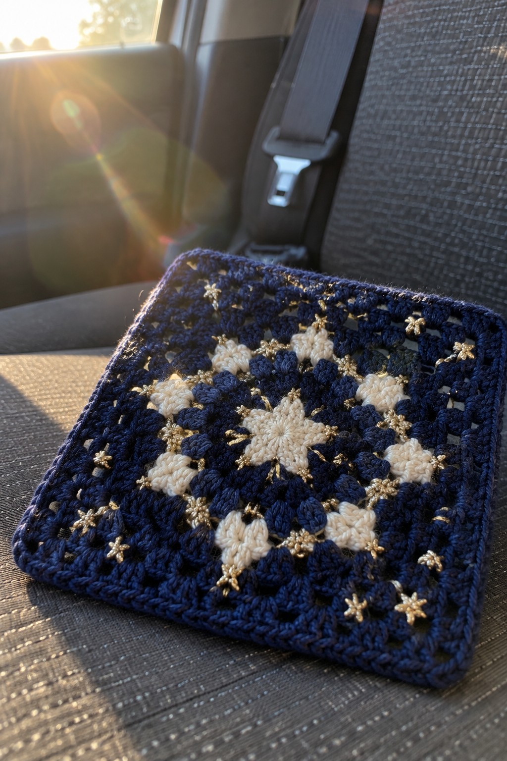 Navy blue crocheted square with white floral motifs and gold stars on car seat