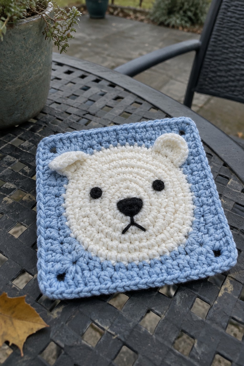 Crocheted white polar bear face on light blue square atop metal table