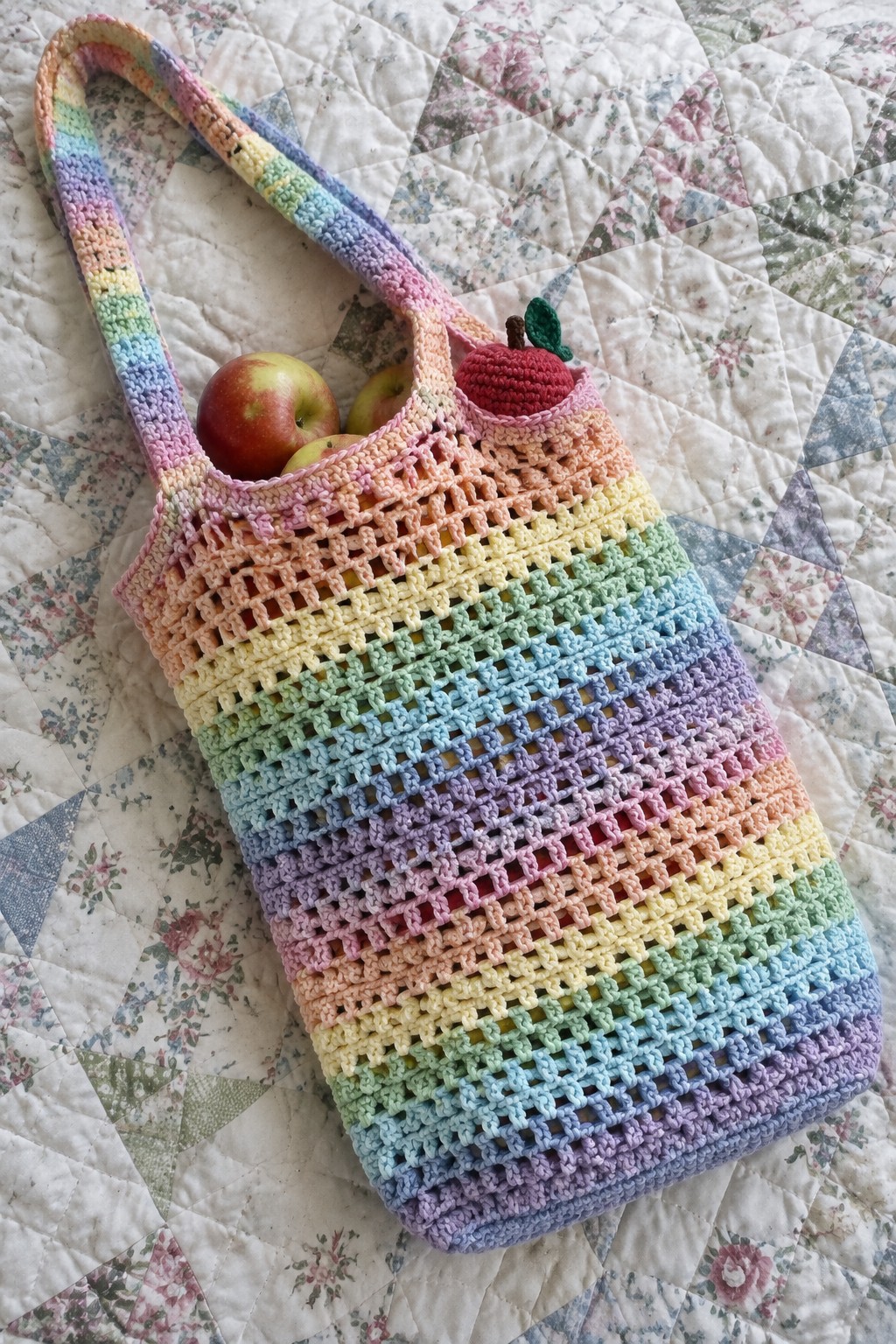 Rainbow crocheted mesh tote bag with apples on floral quilt