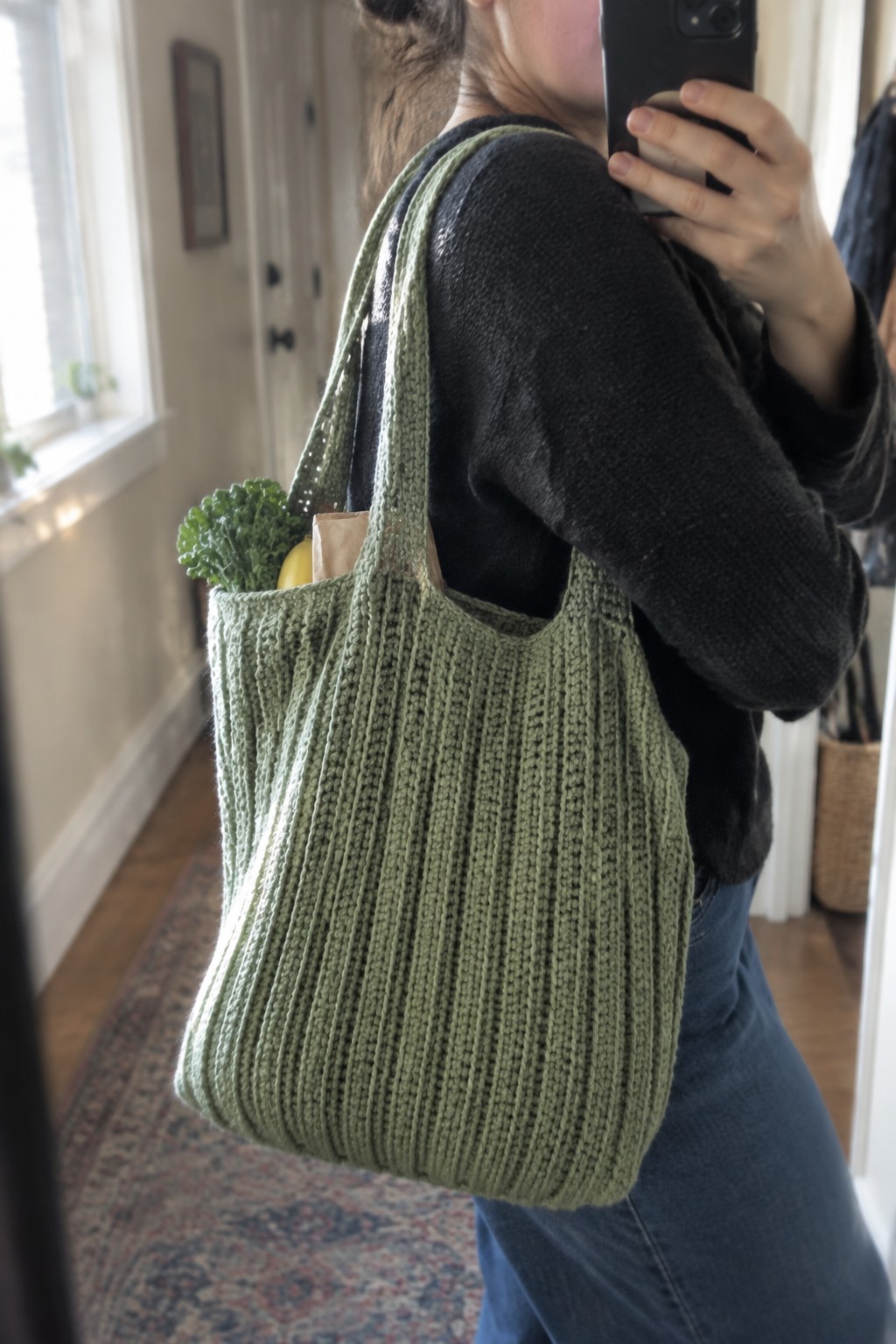 Woman in black sweater with green knitted tote bag holding kale and banana