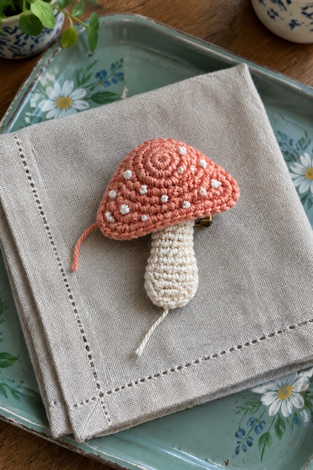 Crocheted peach mushroom brooch with white dots on beige napkin atop floral tray